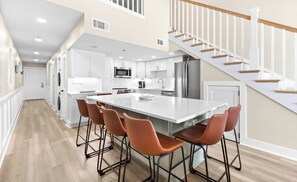 A modern kitchen with white cabinetry, a large island, and a wooden staircase. - Wonderful Gulf-front condo with pool & beach boardwalk in the heart of Destin (Destin)