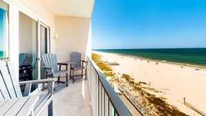 En balkon med Adirondack-stole med udsigt over en strand med en træpromenade og parasoller.