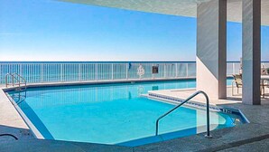 En pool med klart, blåt vand, et hvidt gelænder og udsigt til havet.
