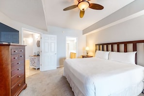 A bedroom with a large bed, a wooden dresser, a ceiling fan, and a television on a stand. - Lovely condo with pool, hot tub, ocean views & pickleball (Santa Rosa Beach)