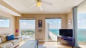 A spacious living room with a large window overlooking a beach and a cityscape. - High-rise condo at beachfront resort w/ pools, hot tubs & arcade (Panama City Beach)