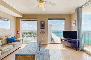 A spacious living room with a large window overlooking a beach and a cityscape. - High-rise condo at beachfront resort w/ pools, hot tubs & arcade (Panama City Beach)