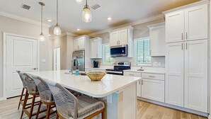 A modern kitchen with white cabinets, a large island with bar stools, stainless steel appliances, and pendant lighting. - Gorgeous townhouse, plenty of space, lots of games, shared pool, close to beach (Perdido Key)