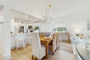A modern kitchen with white cabinetry, a wooden dining table, and a chandelier. - 2nd-floor condo with beach access, pool, tennis, pickleball, hot tub, balcony (Seacrest)