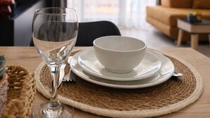 Een eettafel met een glas, een kom en borden op een geweven tafelmat.