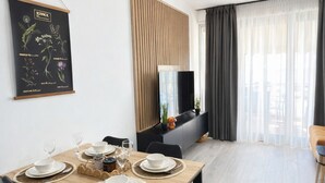 Een moderne eetruimte met een houten tafel voor vier personen, zwarte stoelen en een zwarte tv-meubel op de achtergrond.
