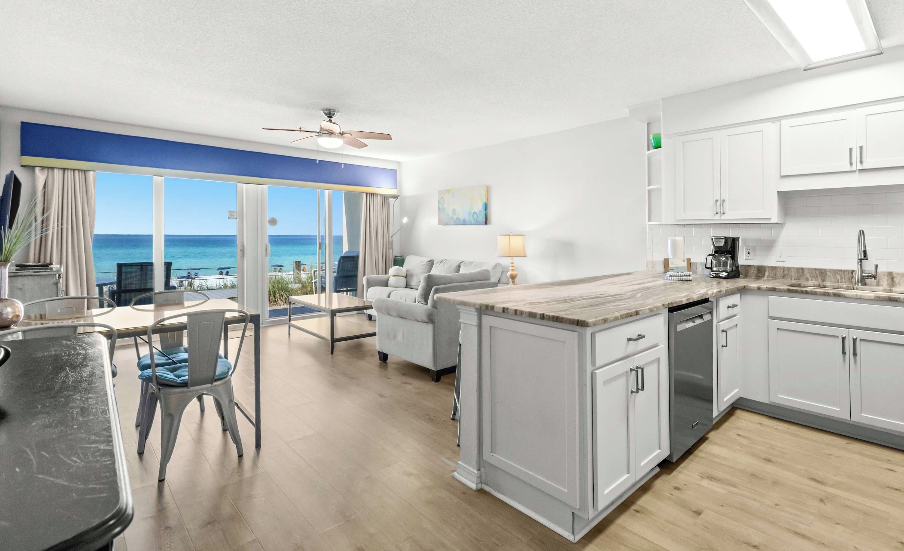 A modern kitchen with white cabinets, a marble countertop, and a view of the ocean.