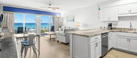 A modern kitchen with white cabinets, a marble countertop, and a view of the ocean.