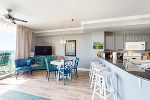 Ein modernes Wohnzimmer mit Sofa, Esstisch und Stühlen, eine Küche mit Mikrowelle und Schränken sowie ein Balkon mit Blick.