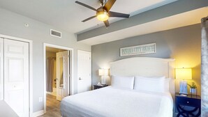 Ein Schlafzimmer mit einem großen Bett, einem Deckenventilator, einem Nachttisch mit Lampe und einem Schild an der Wand.