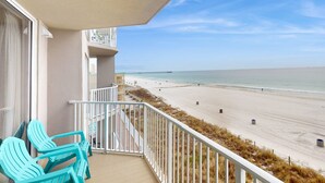 Un balcon avec des chaises turquoise donnant sur une plage et une jetée.