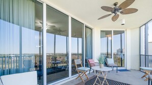 A balcony with a ceiling fan, a white sofa, and a small table with chairs. - Golf getaway near the beach with shared pool, balcony, & WiFi - gorgeous view (Perdido Key)