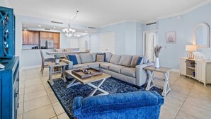 A spacious living room with a sectional sofa, a coffee table, and a dining area with a kitchen in the background. - Golf getaway near the beach with shared pool, balcony, & WiFi - gorgeous view (Perdido Key)