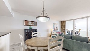 A dining area with a round table, chairs, and a hanging light fixture. There is a sofa and a cabinet in the background.