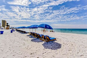 A beach with rows of blue umbrellas and lounge chairs, a sandy shore, and a clear blue sky. - Resort condo near beach with private balcony, WiFi, pool, tennis & dock (Panama City Beach)