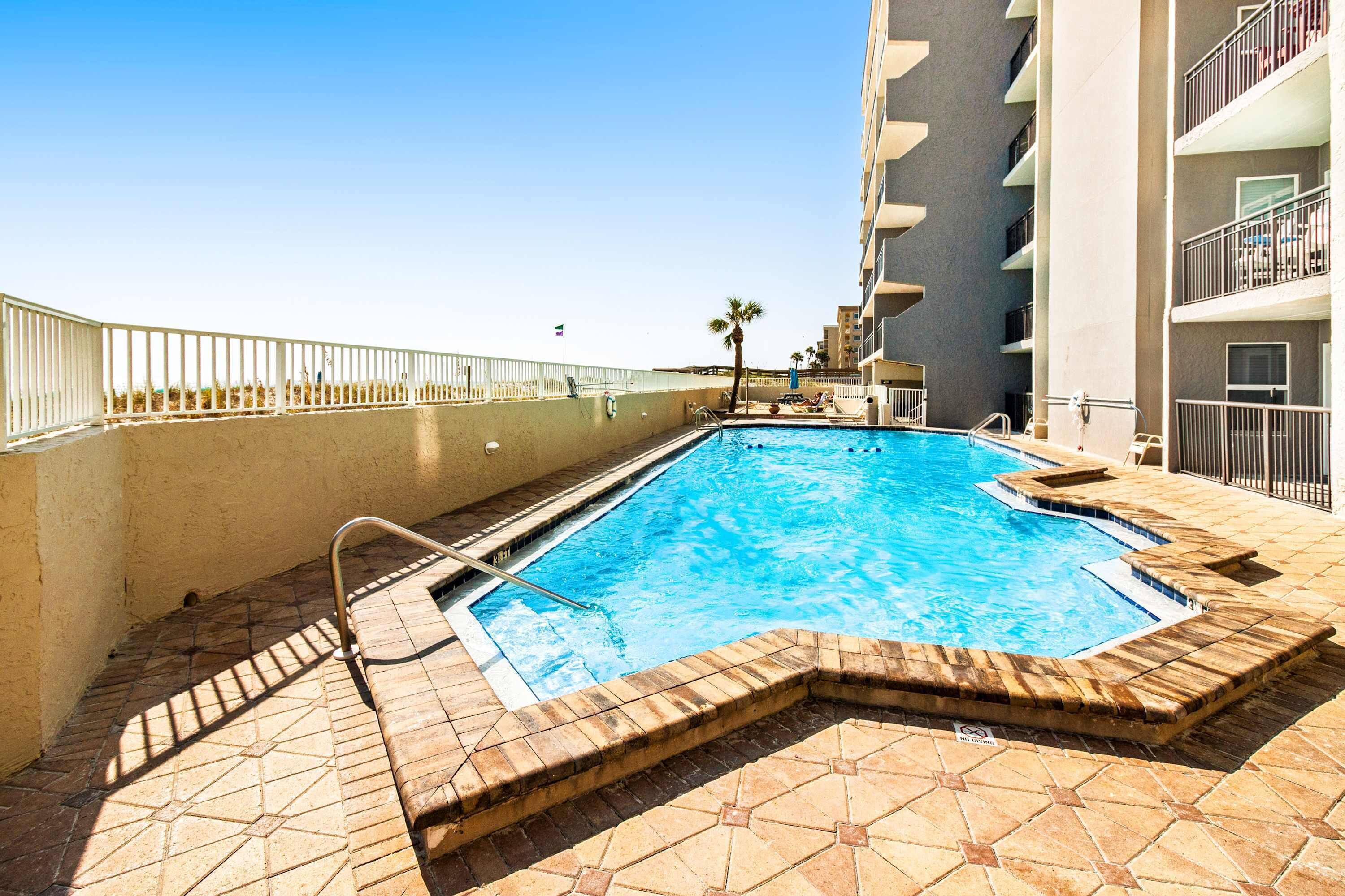 A swimming pool with a tiled deck, a metal ladder, and a white railing.
