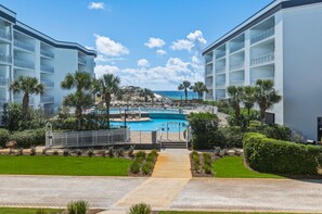 A resort with a swimming pool, palm trees, and a view of the ocean. - Attractive home with spacious balcony, pool view & pickleball - near beach (Santa Rosa Beach)