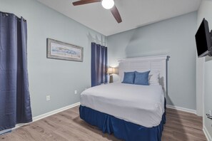 A bedroom with a bed, a ceiling fan, a nightstand, a lamp, and a framed picture on the wall. - Attractive home with spacious balcony, pool view & pickleball - near beach (Santa Rosa Beach)