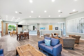 A spacious living area with a dining set, sofas, and a kitchen in the background. - Attractive home with spacious balcony, pool view & pickleball - near beach (Santa Rosa Beach)