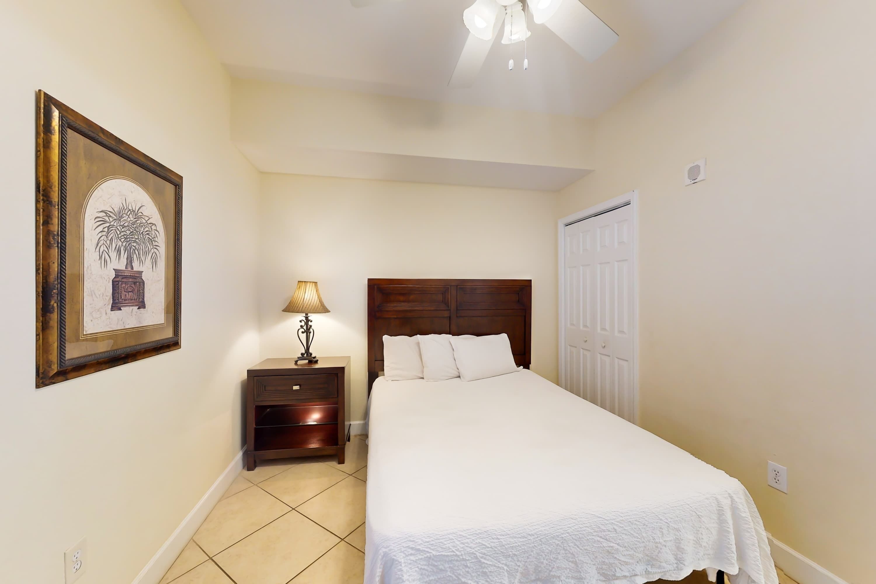 A bedroom with a bed, nightstand, lamp, and a framed picture on the wall.