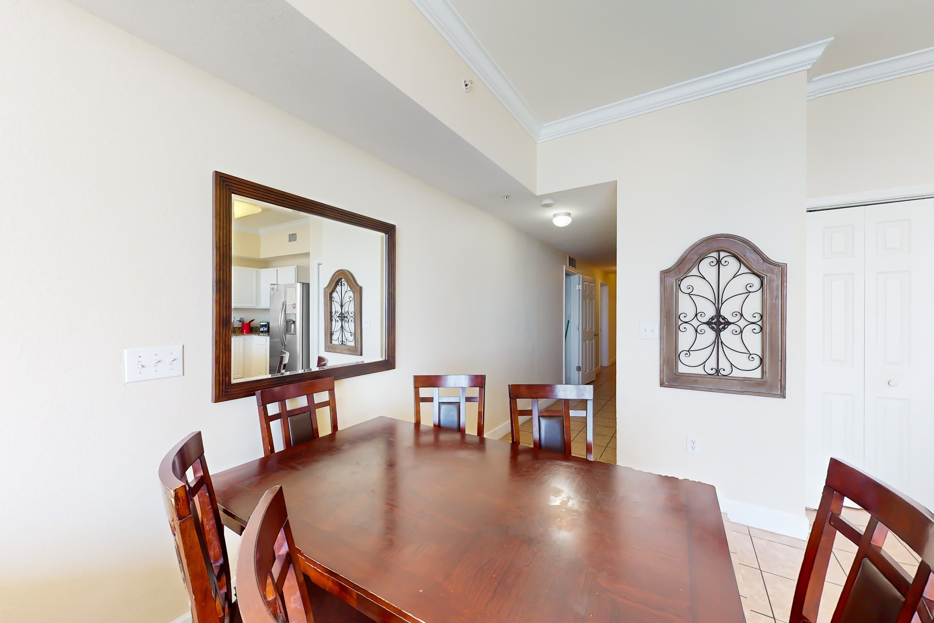 A dining room with a wooden table and chairs, a large mirror, and a decorative wall piece.