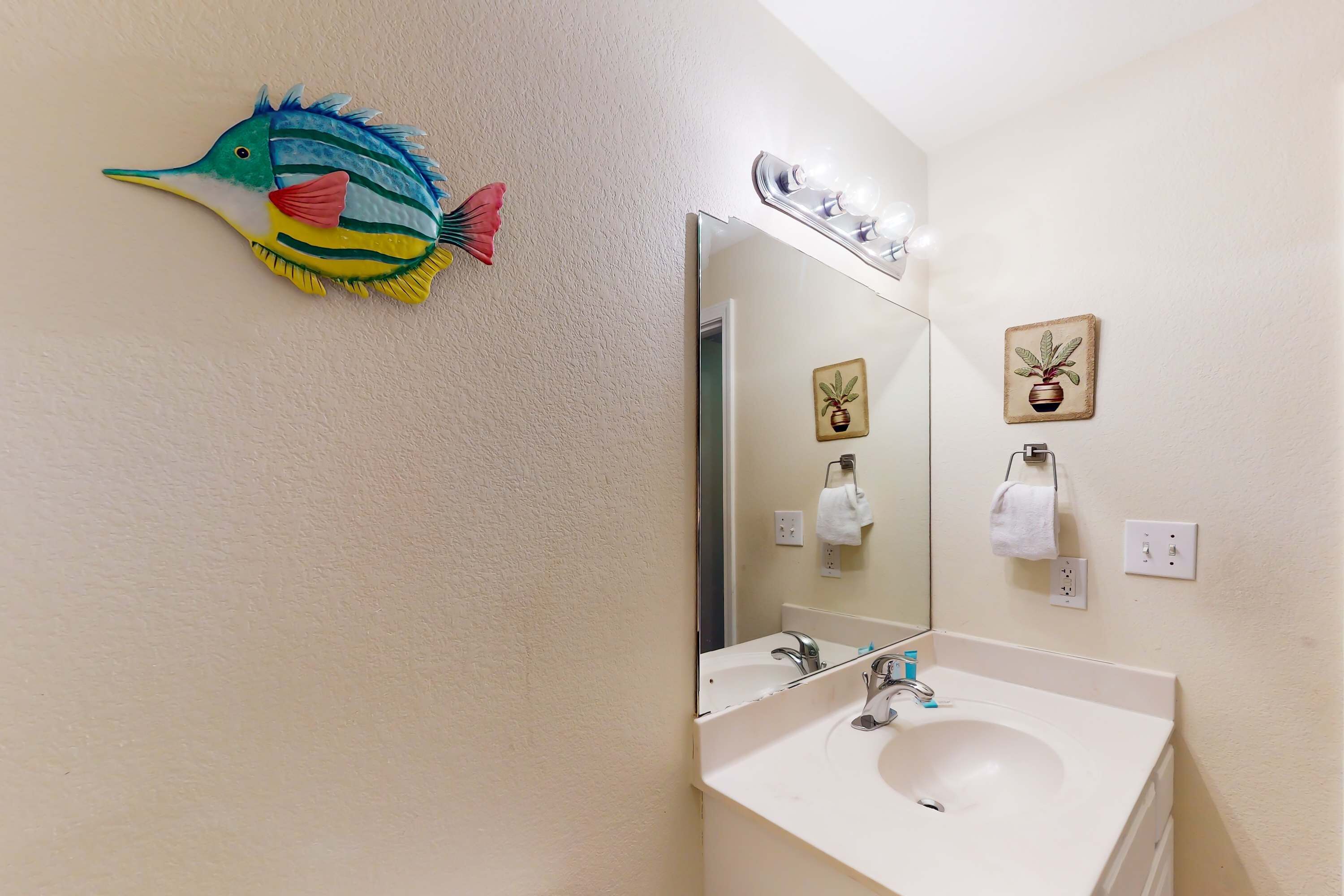 A bathroom with a sink, mirror, and decorative fish on the wall.