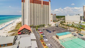 Ein Hochhaus-Hotel mit Blick auf den Strand, einem Parkplatz und einem Tennisplatz.