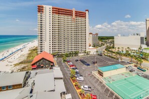 Een hoog hotel met uitzicht op het strand, een parkeerplaats en een tennisbaan.