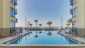 Ein Pool mit Blick auf den Ozean, umgeben von Palmen und einem Gebäude mit Balkonen.