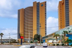 A high-rise hotel with a curved facade, a prominent blue logo, and a sign for Alvin's Island. - Newly renovated oceanfront condo w/ pool & hot tub, ocean view, fast WiFi (Panama City Beach)