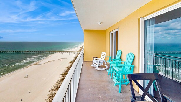 Un balcone con vista sulla spiaggia e sull'oceano. Si vedono sedie turchesi e una sedia nera.