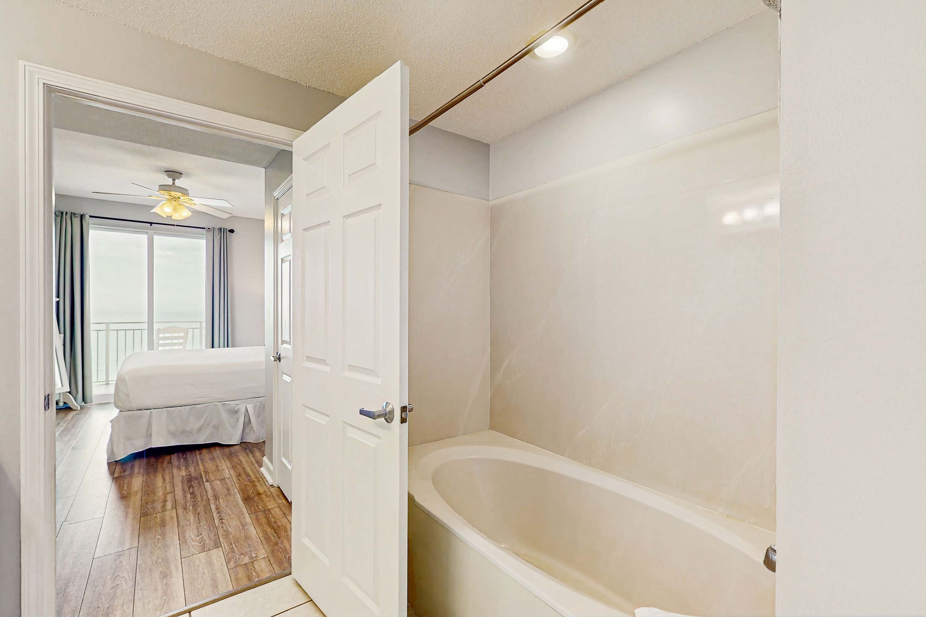A bedroom with a bed, a ceiling fan, and a view of a balcony.