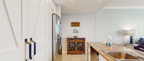 Una cocina con gabinetes blancos, encimera de granito, un lavamanos y un mueble de madera con diseños de palmeras.