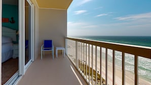 Varanda com vista para o oceano, uma cama, uma cadeira e uma mesa pequena.