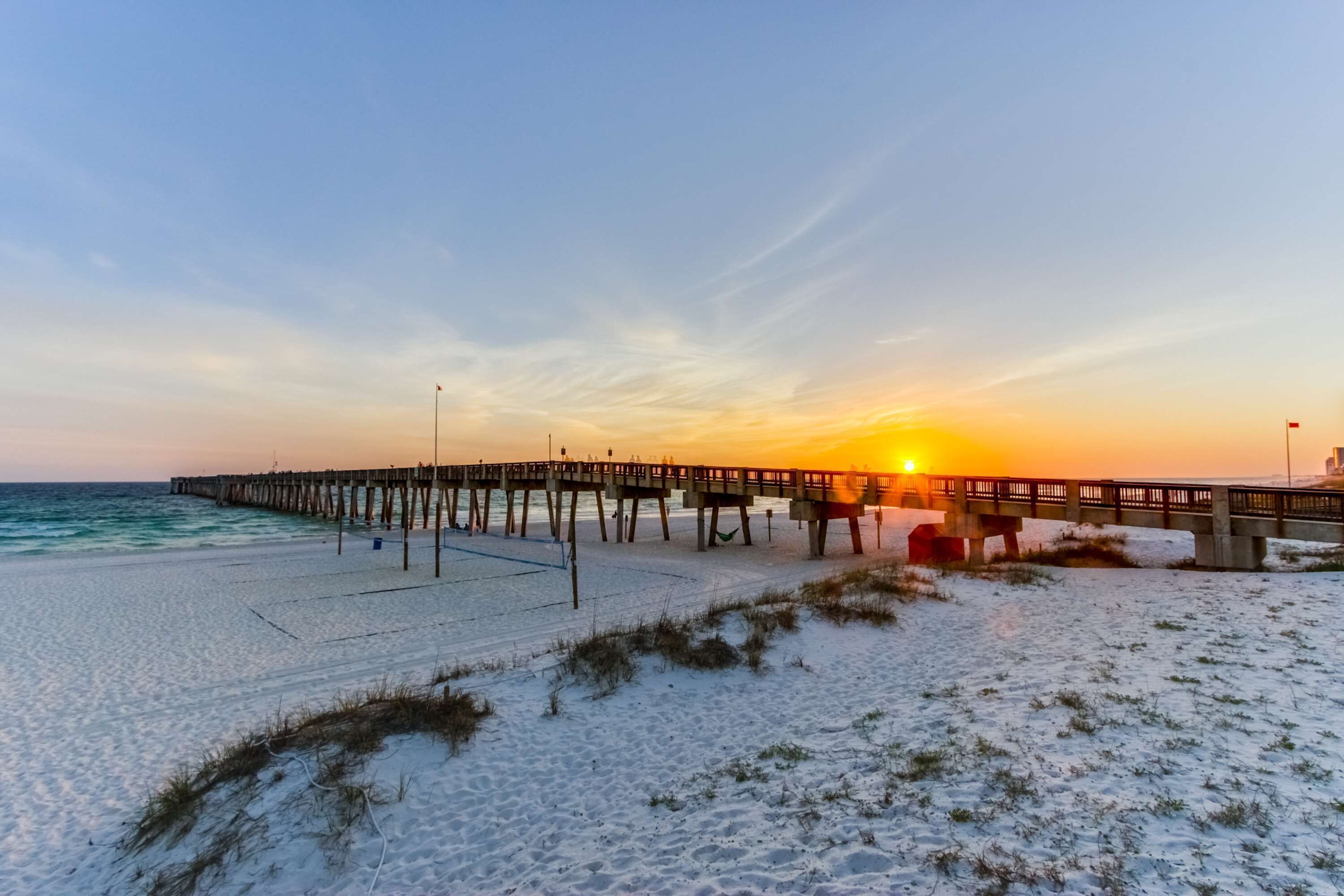 Una playa con un muelle de madera que se adentra en el océano al atardecer.