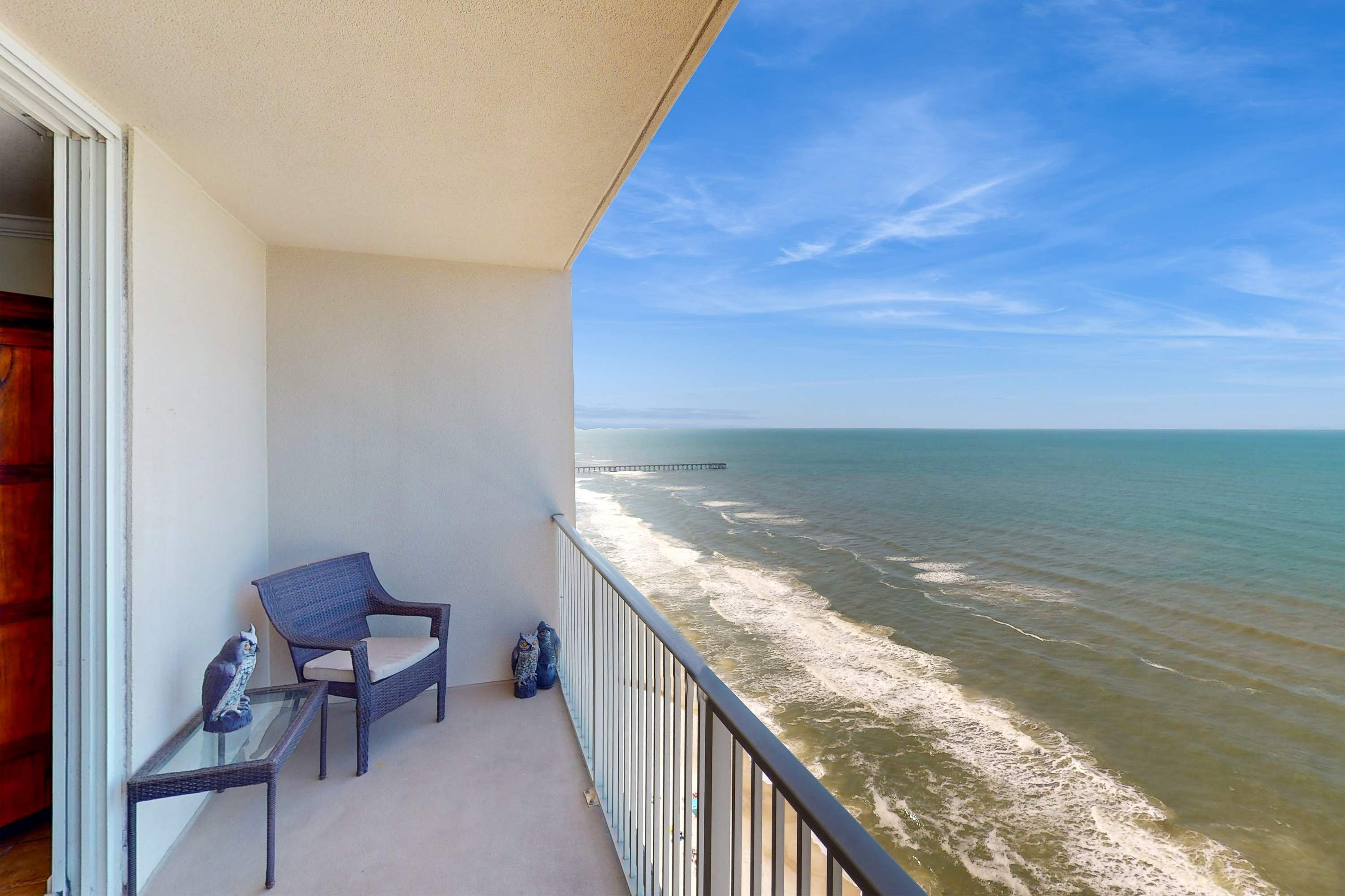 A balcony with a view of the ocean and a pier in the distance.
