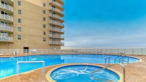 A swimming pool area with a hot tub, surrounded by a brick deck, and adjacent to a high-rise building. - 25th-floor ocean-view condo with pool, hot tub & fast WiFi (Panama City Beach)