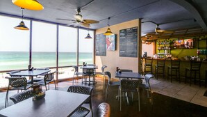 An indoor dining area with tables and chairs, a bar area with bottles, and a menu board. - 25th-floor ocean-view condo with pool, hot tub & fast WiFi (Panama City Beach)