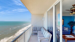 A balcony with a view of the ocean, a sofa, a coffee table, and a blue wall. - 25th-floor ocean-view condo with pool, hot tub & fast WiFi (Panama City Beach)