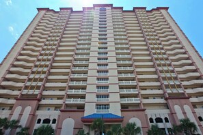 A high-rise building with multiple balconies, a central entrance, and a blue roof. - Water-view beachfront condo with pool - steps to the beach (Panama City Beach)