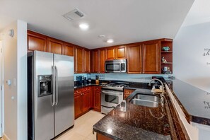 A modern kitchen with wooden cabinets, stainless steel appliances, and a granite countertop. - 5th Floor Lovely Spacious Condo At Waterscape Waterfall, Lazy River (Fort Walton Beach)