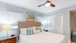 Ein Schlafzimmer mit Bett, Nachttischen, Deckenventilator und Fenster mit Jalousien.