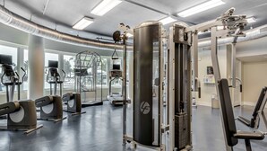 A gym with various exercise machines, a large central machine, and a window providing natural light. - Stunning, Spacious Condo At Waterscape Steps To Beach Lazy River (Fort Walton Beach)