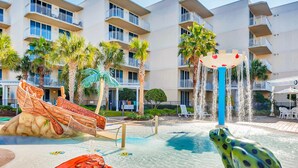 A hotel pool area with a water slide, a frog statue, and a palm tree. - Stunning, Spacious Condo At Waterscape Steps To Beach Lazy River (Fort Walton Beach)