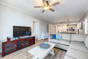 A living room with a TV, sofa, and a dining area with a kitchen in the background. - 3rd Floor Upscale, Welcoming Condo At Waterscape Waterfall, Lazy River (Fort Walton Beach)