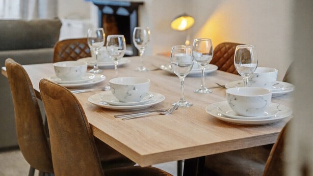 Een eettafel gedekt met witte kommen en wijnglazen, omringd door bruine gestoffeerde stoelen.