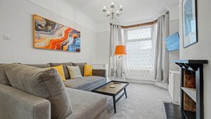 Een moderne woonkamer met een grijze bank, een salontafel, een schilderij, een lamp en een open haard.