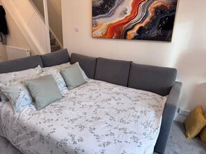 A bedroom with a grey sofa bed, a floral bedspread, and a large abstract painting on the wall.