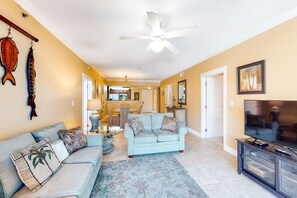 A living room with a light blue sofa, a coffee table, and a TV on a stand. - Cute, coastal condo with lazy river, Gulf view, hot tub & gym - near the beach (Fort Walton Beach)