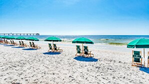 Une plage bordée de rangées de parasols verts et de chaises longues en bois.